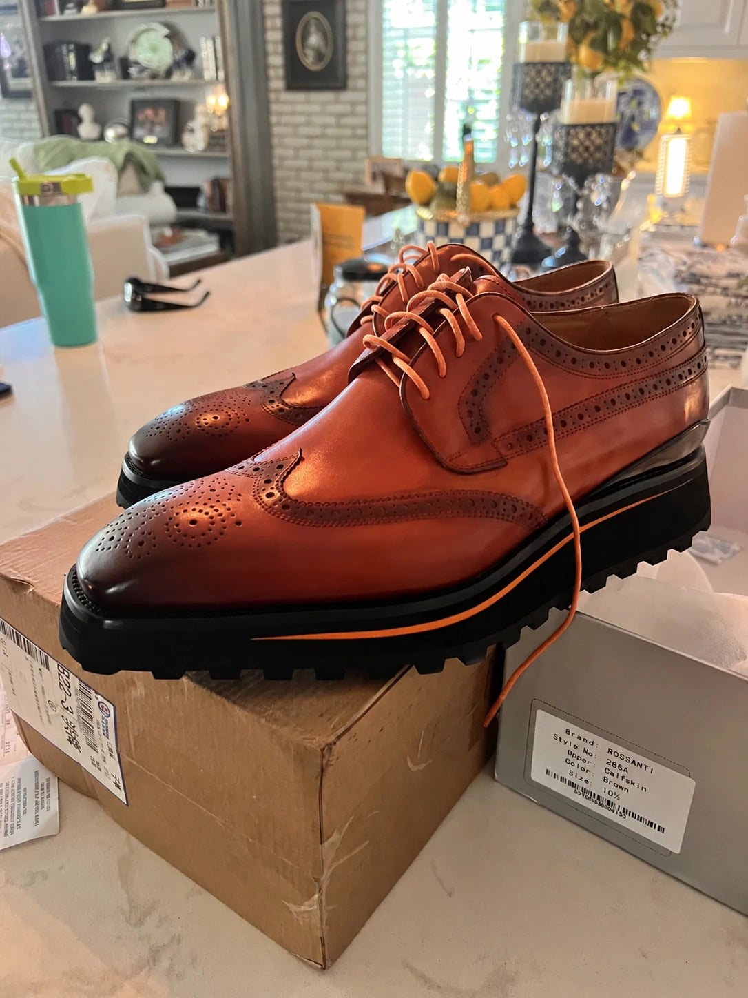 A pair of brown leather wingtip brogues with burnished toes, orange laces and chunky black soles.