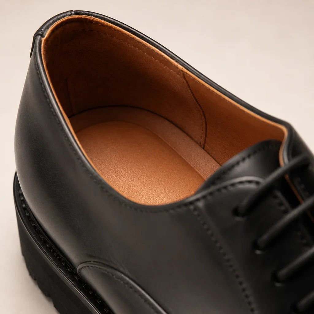 Close-up of a black lace-up shoe showing its tan lining, insole and stitched interior seams.